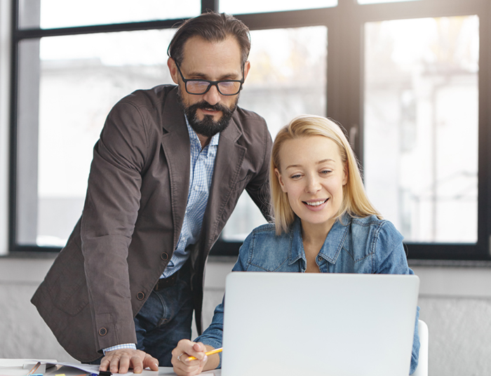 Portrait of female and male coworkers discuss ideas for common project, look at screen of laptop, communicate about strategies. Happy woman shows works results to her boss, being encouraged.